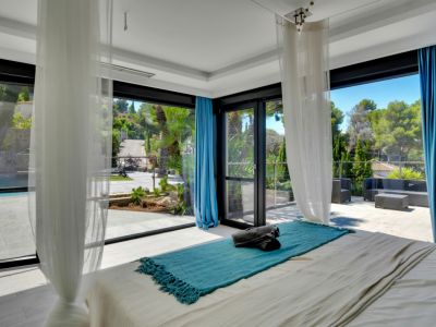 Dormitorio luminoso con acceso directo a una amplia terraza exterior, piscina y vistas a la vegetación a través de grandes ventanales de suelo a techo.