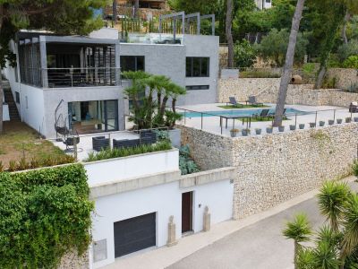 Vista aérea de la villa moderna con piscina privada, terrazas ajardinadas y muros de piedra natural, destacando su diseño multinivel y garaje a pie de calle.