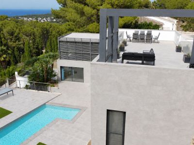 Vista aérea de la villa moderna, destacando la piscina privada de diseño, amplias terrazas de gres y una zona chill-out elevada con vistas al mar Mediterráneo y la vegetación. Diseño contemporáneo.