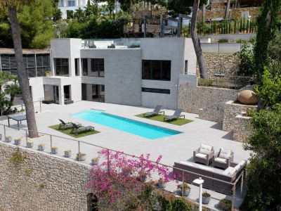 Vista aérea de la villa moderna, destacando su elegante fachada gris, piscina privada rectangular y amplias terrazas de gres. Muros de piedra y vegetación mediterránea enmarcan la propiedad.