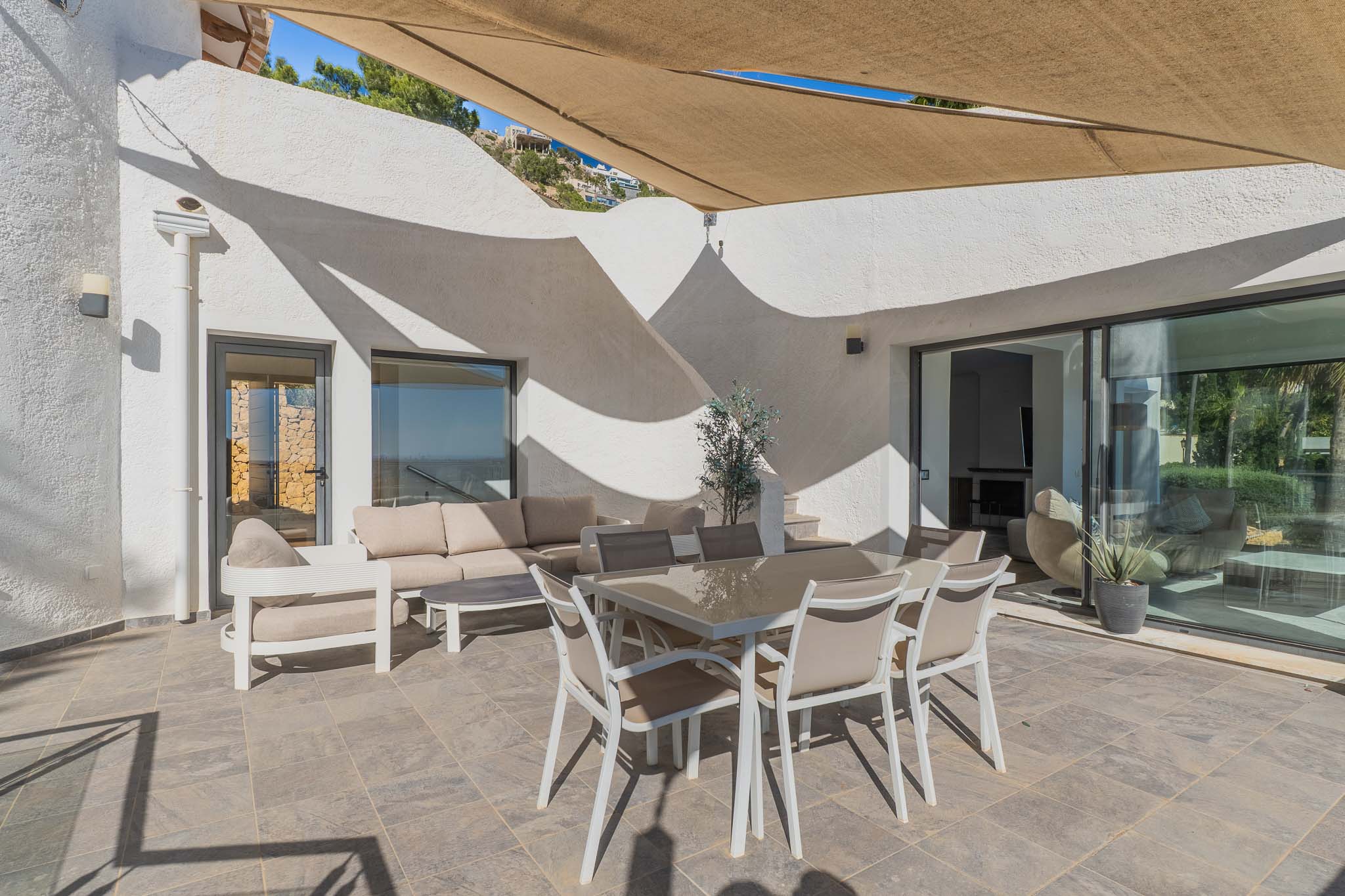 Amplia terraza exterior con suelo de gres, mobiliario de comedor y zona lounge bajo toldo retráctil. Grandes ventanales conectan con el interior. Amplia terraza exterior con suelo de gres, mobiliario de comedor y zona lounge bajo toldo retráctil. Grandes ventanales conectan con el interior.