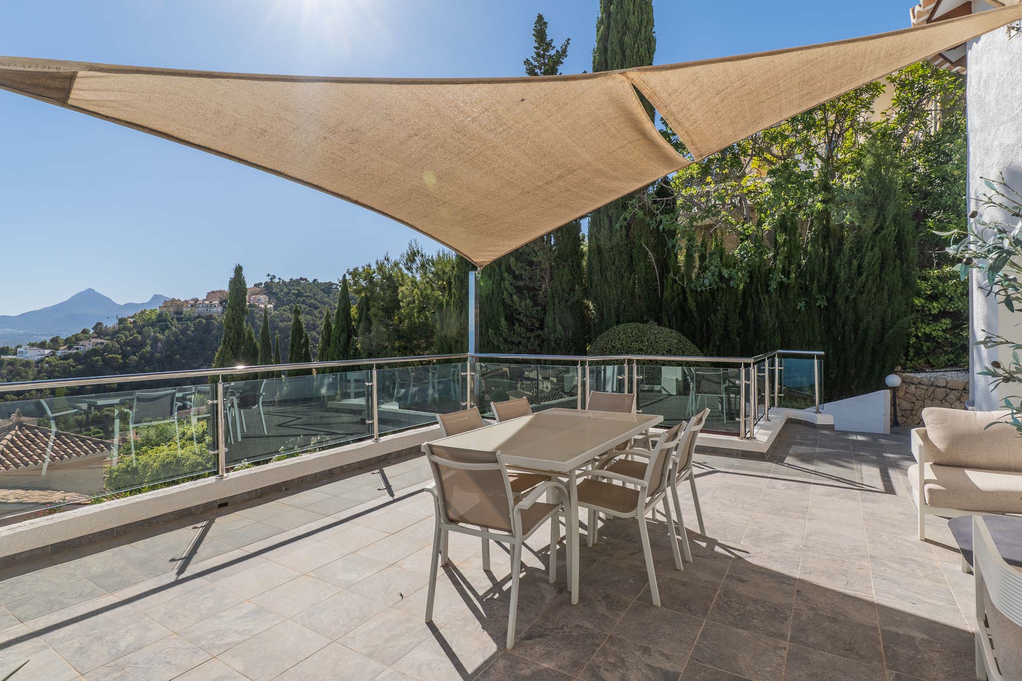 Amplia terraza exterior con vela de sombra, equipada con mesa de comedor y barandilla de cristal, ofreciendo vistas panorámicas a las montañas y la urbanización. Amplia terraza exterior con vela de sombra, equipada con mesa de comedor y barandilla de cristal, ofreciendo vistas panorámicas a las montañas y la urbanización.