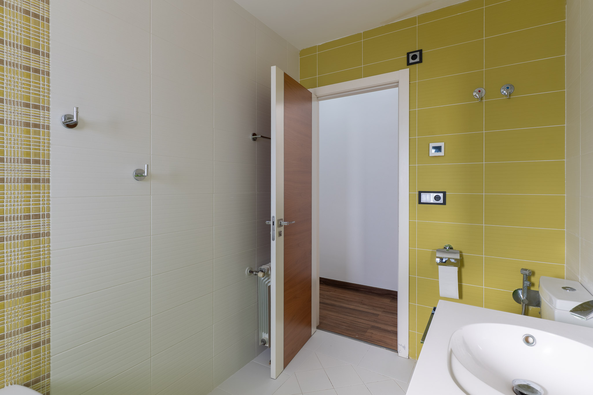 Baño de cortesía con diseño moderno, destacando azulejos en tonos beige y verde lima, un lavabo contemporáneo y detalles en cromo. La puerta de madera entreabre a un espacio con suelo de parquet. Baño de cortesía con diseño moderno, destacando azulejos en tonos beige y verde lima, un lavabo contemporáneo y detalles en cromo. La puerta de madera entreabre a un espacio con suelo de parquet.