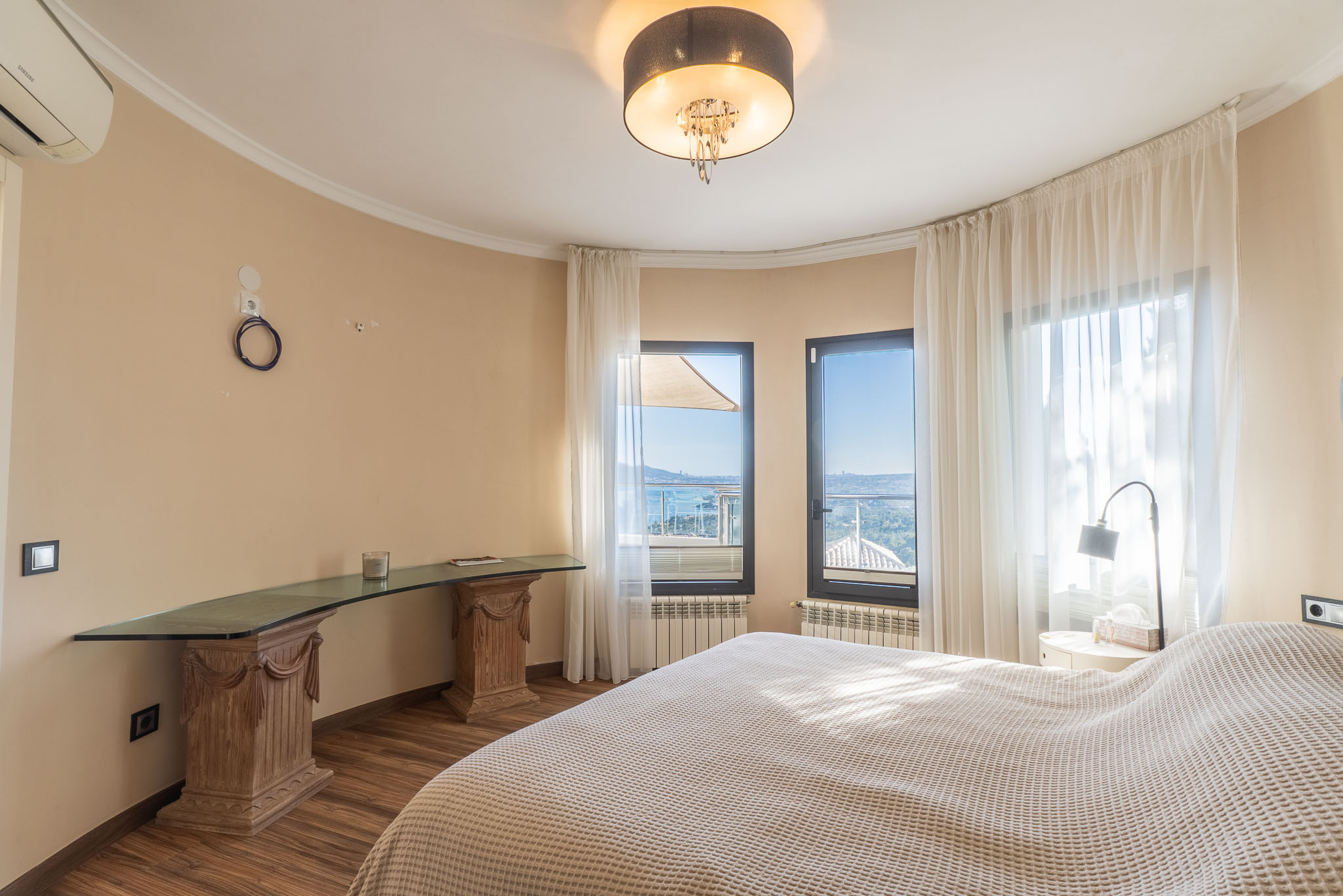 Dormitorio luminoso con vistas panorámicas al mar a través de amplios ventanales, complementado por un escritorio de cristal sobre pedestales de madera tallada. Dormitorio luminoso con vistas panorámicas al mar a través de amplios ventanales, complementado por un escritorio de cristal sobre pedestales de madera tallada.