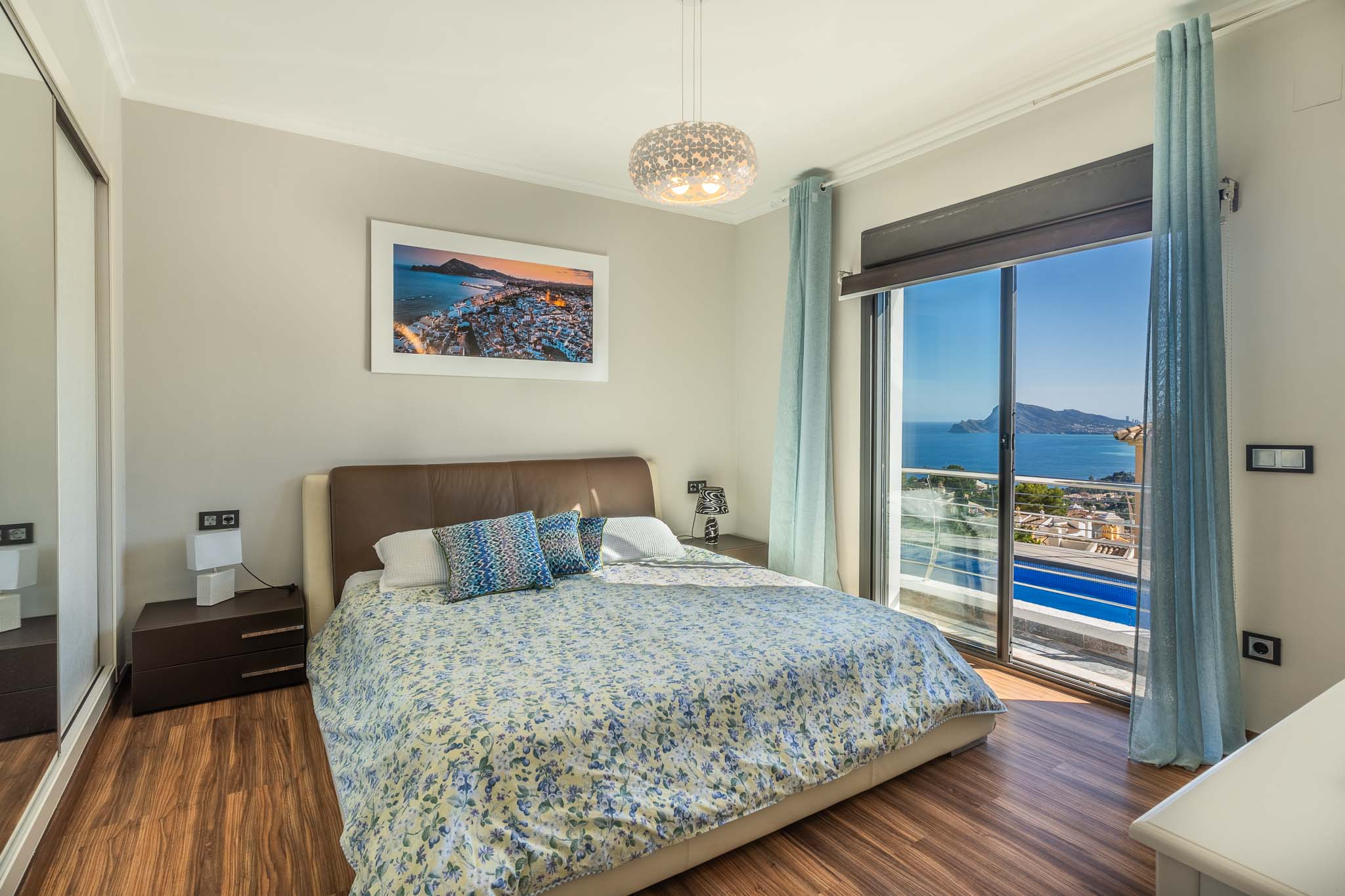 Dormitorio principal con cama doble, suelo laminado de madera y vistas panorámicas al mar desde el ventanal. Incluye armario espejado y mobiliario moderno. Dormitorio principal con cama doble, suelo laminado de madera y vistas panorámicas al mar desde el ventanal. Incluye armario espejado y mobiliario moderno.