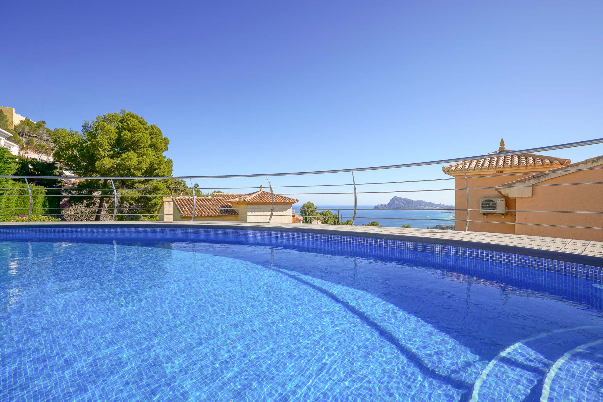 Piscina de mosaico azul con escalones integrados y barandilla moderna, ofreciendo vistas panorámicas al mar, tejados tradicionales y la costa. Piscina de mosaico azul con escalones integrados y barandilla moderna, ofreciendo vistas panorámicas al mar, tejados tradicionales y la costa.