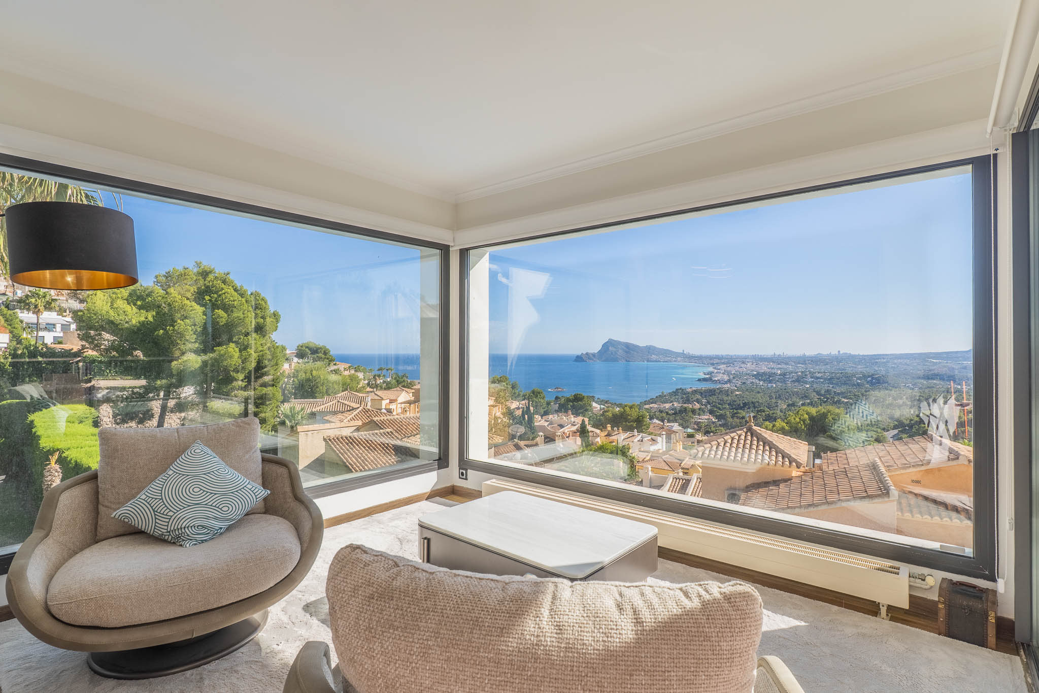 Salón con amplios ventanales de esquina que ofrecen vistas panorámicas al mar y la costa. Dos sillones y una mesa de centro moderna crean un espacio luminoso para el relax. Salón con amplios ventanales de esquina que ofrecen vistas panorámicas al mar y la costa. Dos sillones y una mesa de centro moderna crean un espacio luminoso para el relax.