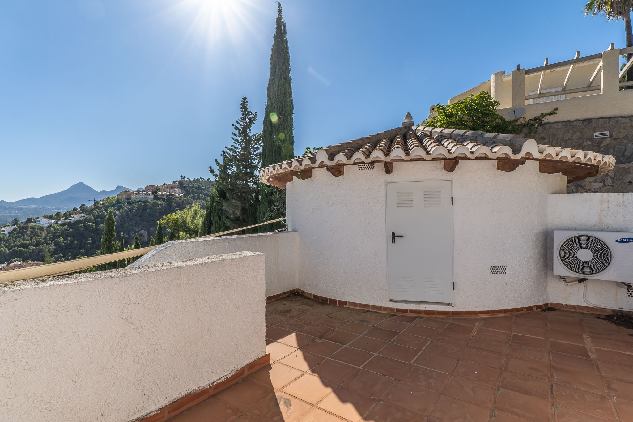 Terraza de baldosas de terracota con un encantador edificio auxiliar de tejado tradicional. Ofrece vistas panorámicas a las verdes colinas y montañas lejanas bajo un cielo despejado. Terraza de baldosas de terracota con un encantador edificio auxiliar de tejado tradicional. Ofrece vistas panorámicas a las verdes colinas y montañas lejanas bajo un cielo despejado.
