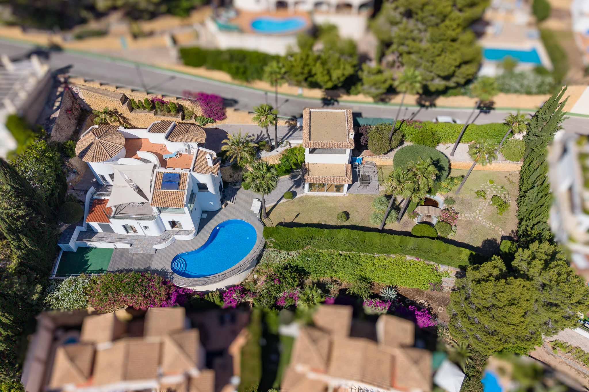 Vista aérea de la villa con su piscina de forma irregular, amplios jardines llanos con estanque y un edificio anexo. Destacan los tejados de teja y la abundante vegetación mediterránea. Vista aérea de la villa con su piscina de forma irregular, amplios jardines llanos con estanque y un edificio anexo. Destacan los tejados de teja y la abundante vegetación mediterránea.