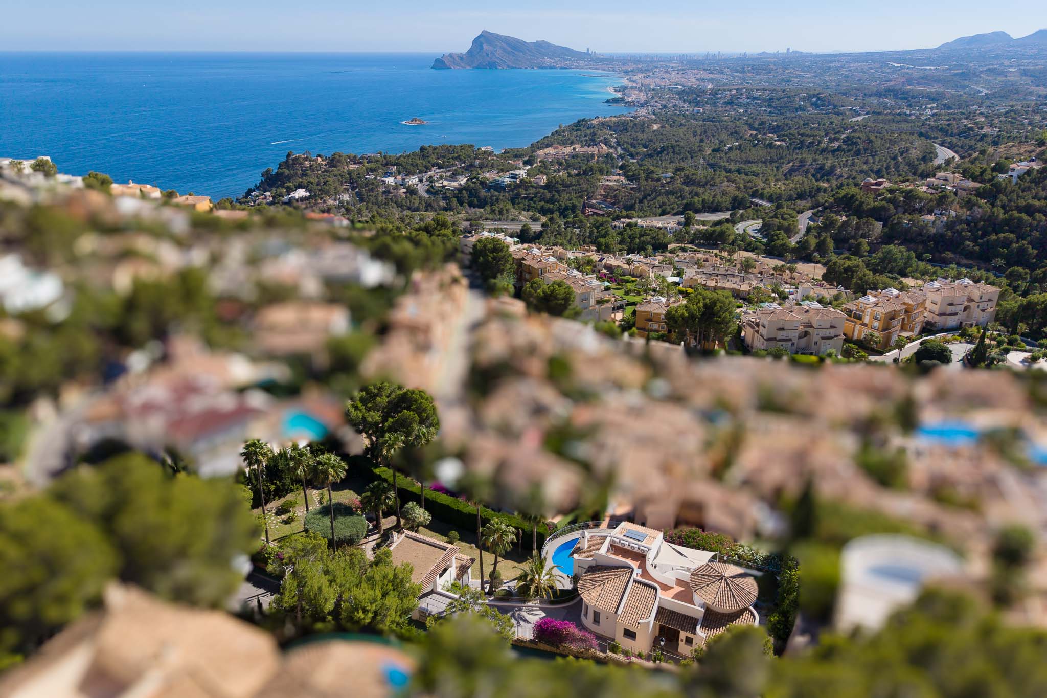 Vista aérea de una villa en Altea Hills con piscina curva, tejados de terracota y jardines exuberantes, enmarcada por el Mediterráneo y la costa. Vista aérea de una villa en Altea Hills con piscina curva, tejados de terracota y jardines exuberantes, enmarcada por el Mediterráneo y la costa.