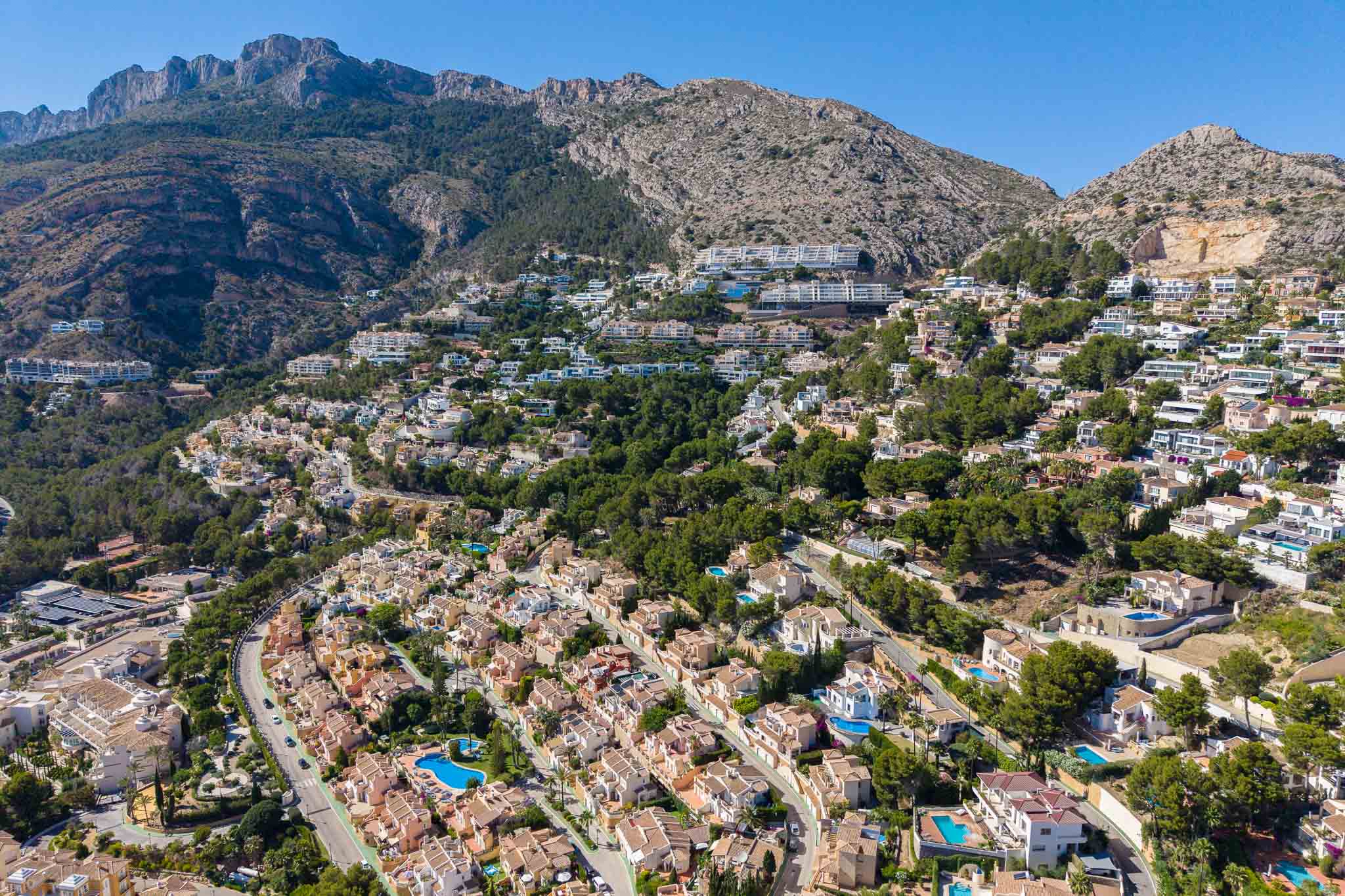 Vista aérea panorámica de Altea Hills, mostrando numerosas villas con piscinas en la ladera verde, con majestuosas montañas al fondo. Vista aérea panorámica de Altea Hills, mostrando numerosas villas con piscinas en la ladera verde, con majestuosas montañas al fondo.
