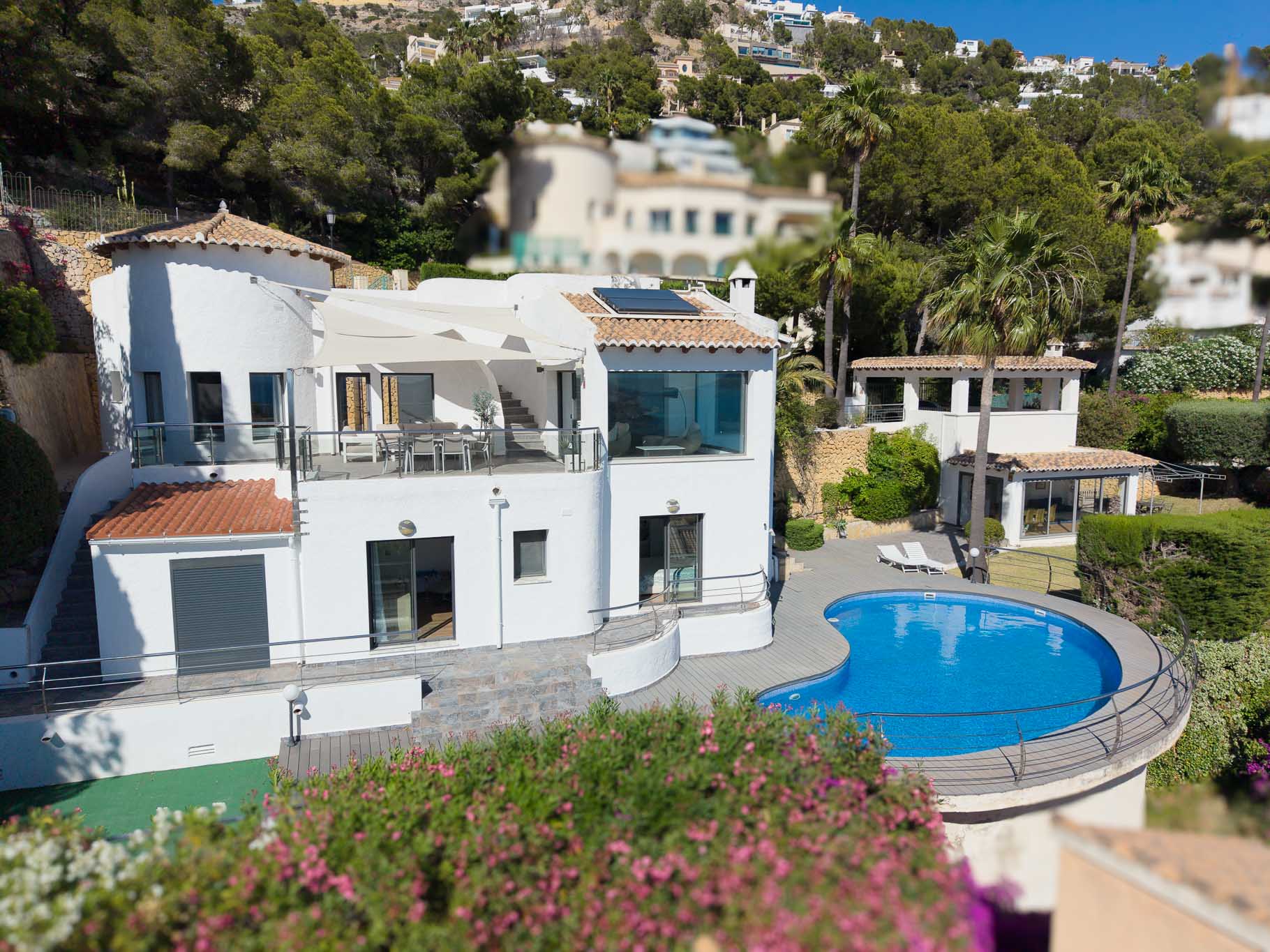 Vista elevada de la villa principal, con una amplia terraza superior con comedor y toldo, piscina en forma de riñón con tarima y una casa de invitados separada, todo rodeado de exuberante paisaje mediterráneo. Vista elevada de la villa principal, con una amplia terraza superior con comedor y toldo, piscina en forma de riñón con tarima y una casa de invitados separada, todo rodeado de exuberante paisaje mediterráneo.