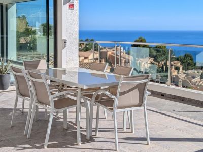 Amplia terraza exterior con mesa de comedor y sillas, ofreciendo vistas panorámicas al mar Mediterráneo y los tejados de Altea Hills. Puertas correderas de cristal conectan con el interior.