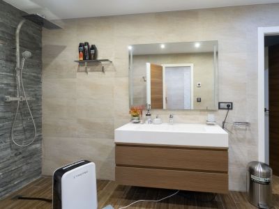 Baño moderno con ducha de lluvia y pared de pizarra, tocador flotante de madera y lavabo integrado. Suelo de baldosas imitación madera.