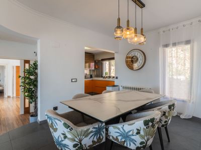 Comedor con mesa de efecto mármol y sillas tapizadas con patrón tropical. La iluminación colgante moderna ilumina el espacio, abierto a una cocina con gabinetes naranjas.