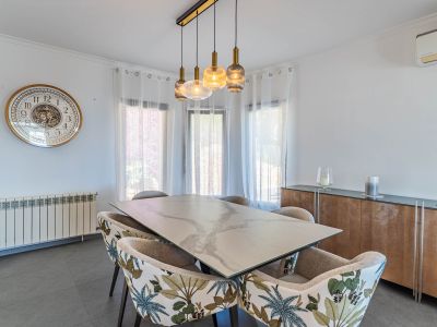 Comedor luminoso con mesa de efecto mármol, sillas de estampado tropical y un moderno candelabro lineal sobre el espacio.