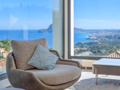 Cómodo sillón junto a ventanal panorámico, ofreciendo vistas ininterrumpidas al mar Mediterráneo y la costa. El cojín decorativo añade un toque moderno al diseño interior.