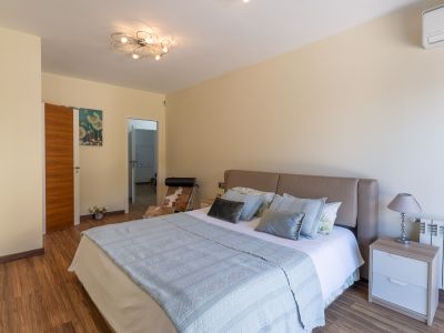 Dormitorio con cama de cabecero beige, suelo laminado de madera y moderna lámpara de techo. Incluye mesita de noche con lámpara, radiador y aire acondicionado.