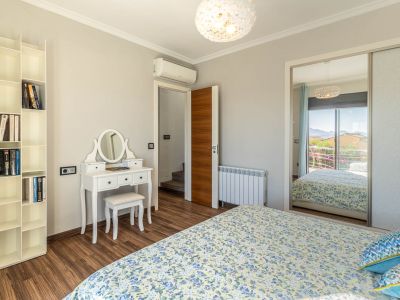 Dormitorio con suelo laminado de madera, tocador blanco y estantería modular. El armario con espejo refleja una vista a la montaña desde el balcón.