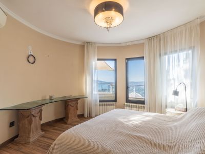 Dormitorio luminoso con vistas panorámicas al mar a través de amplios ventanales, complementado por un escritorio de cristal sobre pedestales de madera tallada.