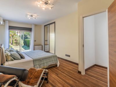 Dormitorio principal con acceso directo al jardín a través de puertas correderas de cristal, suelo laminado y armario empotrado con puertas de espejo. Incluye un espacio de vestidor abierto.