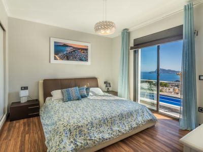 Dormitorio principal con cama doble, suelo laminado de madera y vistas panorámicas al mar desde el ventanal. Incluye armario espejado y mobiliario moderno.