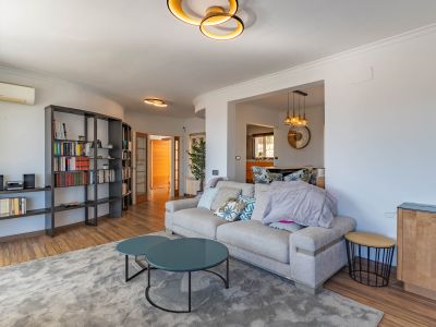 Espacioso salón con sofá contemporáneo, mesas de centro redondas en tono teal y una estantería modular oscura. Destacan la iluminación de diseño y los suelos de madera.