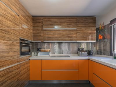 Moderna cocina con armarios superiores de madera veteada brillante y bajos en naranja vibrante, complementada por encimeras claras y un salpicadero de mosaico metálico.