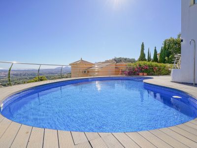 Piscina curva con mosaico azul y tarima de madera clara, enmarcada por una barandilla de acero, ofreciendo vistas panorámicas al valle y ciudad lejana.