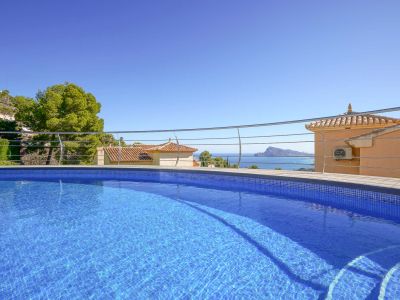 Piscina de mosaico azul con escalones integrados y barandilla moderna, ofreciendo vistas panorámicas al mar, tejados tradicionales y la costa.