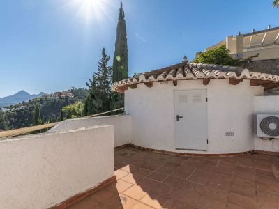 Terraza de baldosas de terracota con un encantador edificio auxiliar de tejado tradicional. Ofrece vistas panorámicas a las verdes colinas y montañas lejanas bajo un cielo despejado.