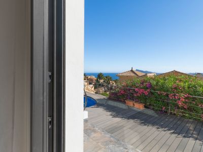 Vista desde la puerta corredera a la terraza con tarima de composite, piscina y barandilla de acero. El mar Mediterráneo y tejados tradicionales se aprecian al fondo.