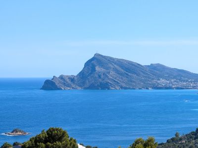 Vista panorámica del Mediterráneo con el imponente perfil de la Sierra Helada, una ciudad costera a lo lejos y pequeños islotes rocosos bajo un cielo azul claro.