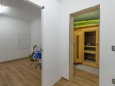 Zona de bienestar con cabina de sauna de madera y bancos interiores, contigua a un cuarto de servicio. Ambos espacios presentan suelo de gres imitación madera.