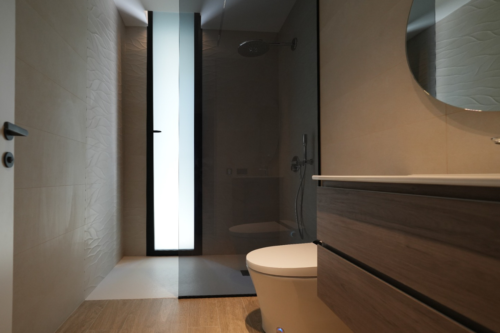 Baño moderno con mueble de madera, espejo redondo y ducha a ras de suelo. Destacan azulejos texturizados y una ventana esmerilada. Baño moderno con mueble de madera, espejo redondo y ducha a ras de suelo. Destacan azulejos texturizados y una ventana esmerilada.