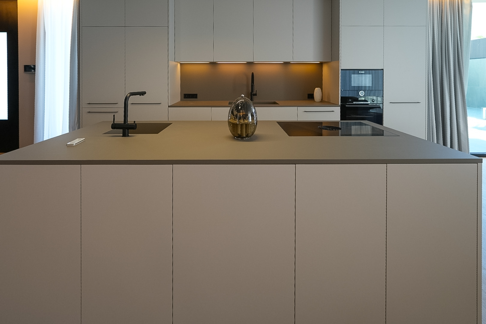 Cocina de diseño con isla central, fregadero integrado, placa de inducción y mobiliario en tonos neutros. Cocina de diseño con isla central, fregadero integrado, placa de inducción y mobiliario en tonos neutros.