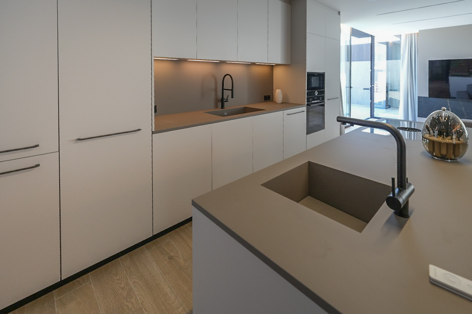 Cocina de diseño con isla central y doble fregadero integrado. Armarios minimalistas en tonos neutros, electrodomésticos empotrados y suelo de madera clara, con acceso directo al exterior. Cocina de diseño con isla central y doble fregadero integrado. Armarios minimalistas en tonos neutros, electrodomésticos empotrados y suelo de madera clara, con acceso directo al exterior.