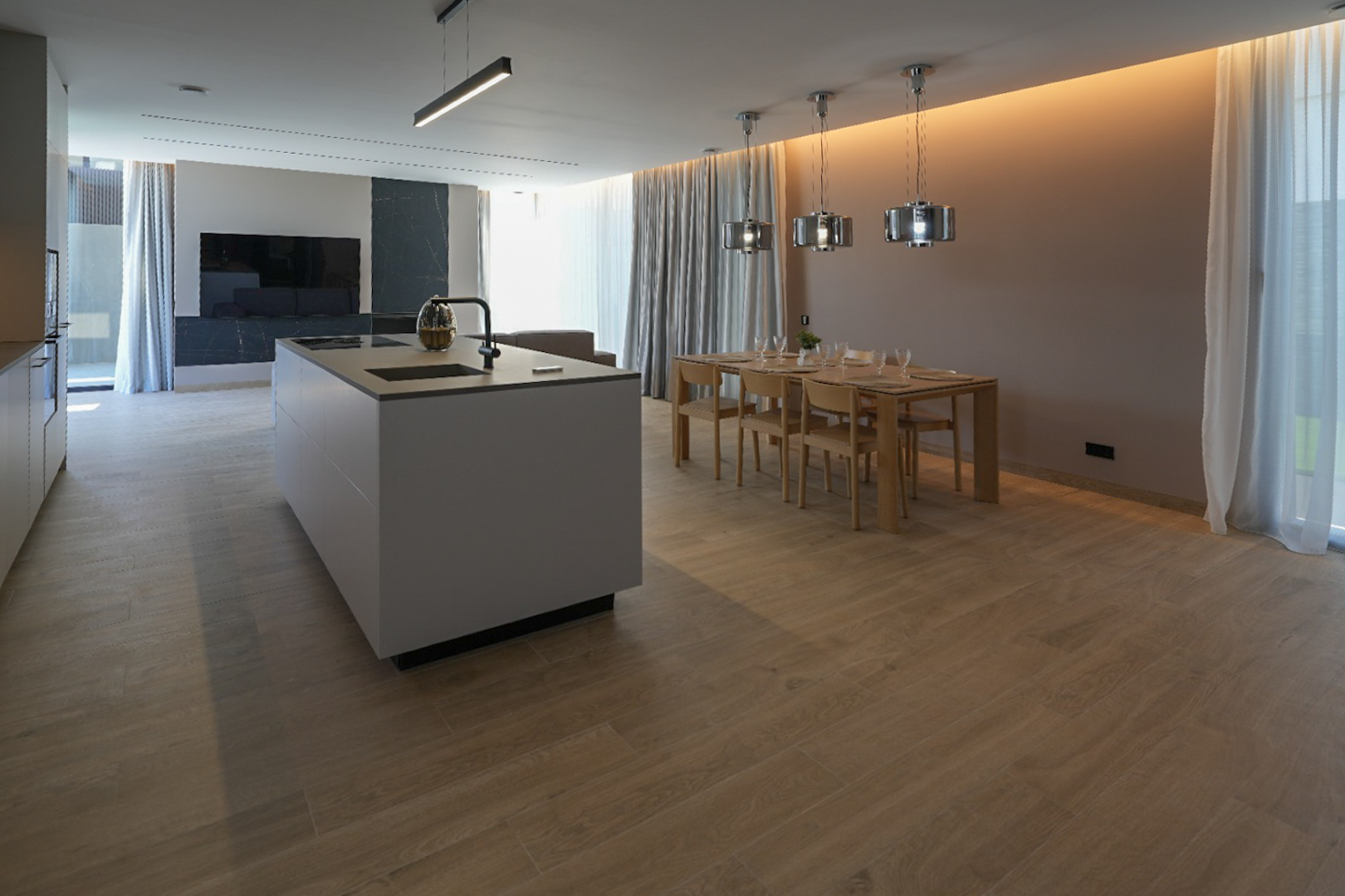 Cocina de diseño con isla central y electrodomésticos integrados, conectada a un comedor con mesa de madera y lámparas colgantes modernas. Suelo de porcelánico efecto madera. Cocina de diseño con isla central y electrodomésticos integrados, conectada a un comedor con mesa de madera y lámparas colgantes modernas. Suelo de porcelánico efecto madera.