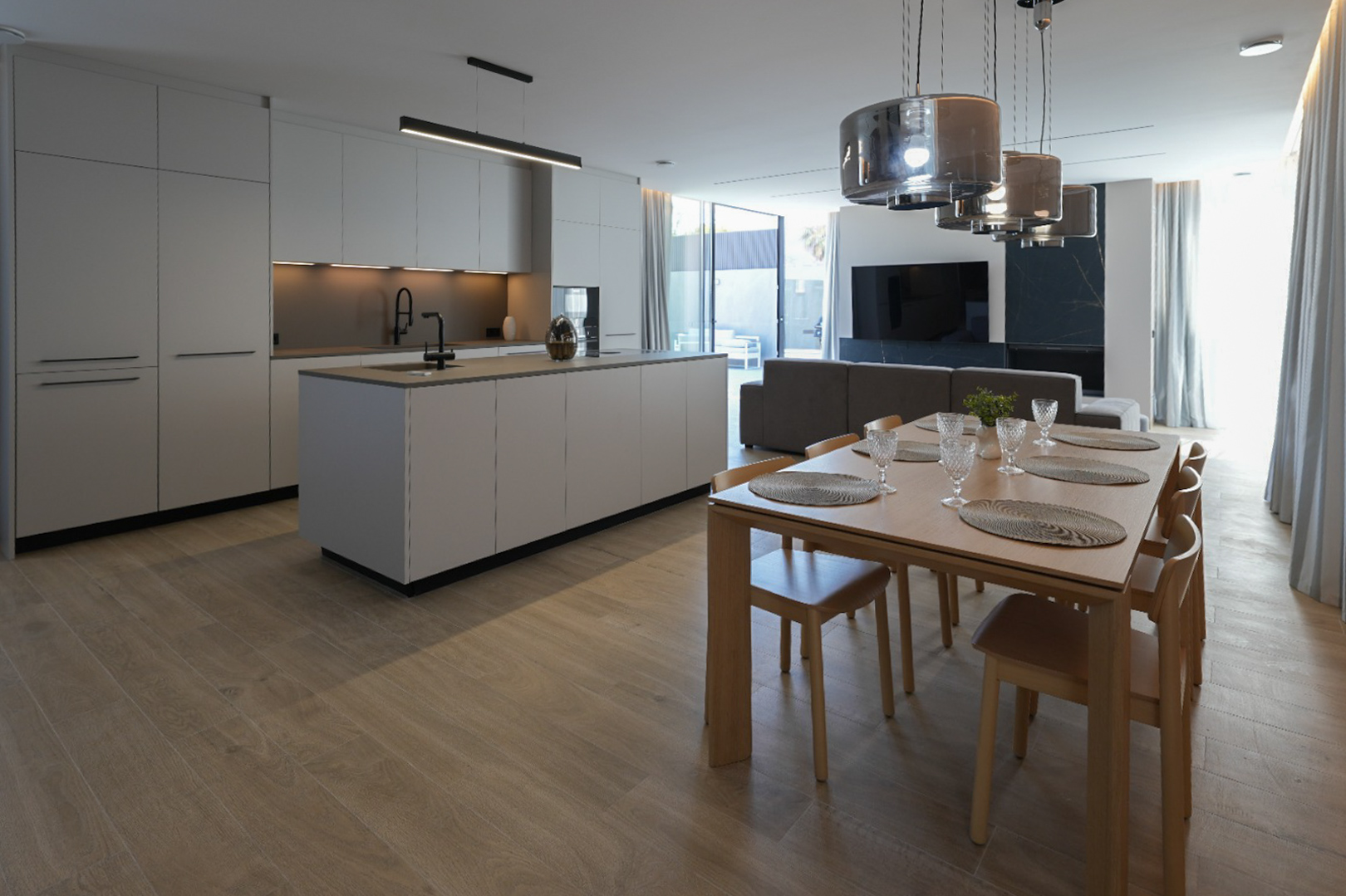 Cocina de diseño minimalista con isla central y grifería negra, abierta a un elegante comedor de madera con seis sillas y lámparas colgantes modernas. Cocina de diseño minimalista con isla central y grifería negra, abierta a un elegante comedor de madera con seis sillas y lámparas colgantes modernas.
