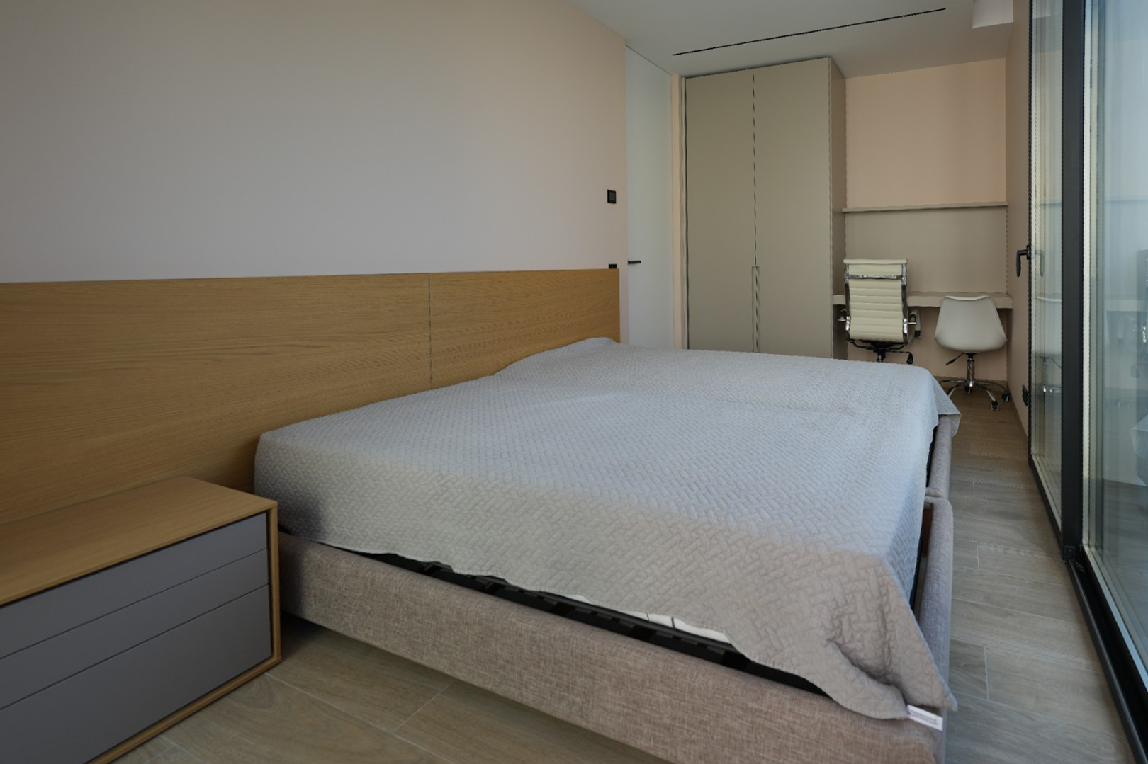 Dormitorio moderno con cama tapizada gris claro, cabecero de madera y mesita integrada. Dispone de armario empotrado, zona de escritorio doble y amplios ventanales. Dormitorio moderno con cama tapizada gris claro, cabecero de madera y mesita integrada. Dispone de armario empotrado, zona de escritorio doble y amplios ventanales.