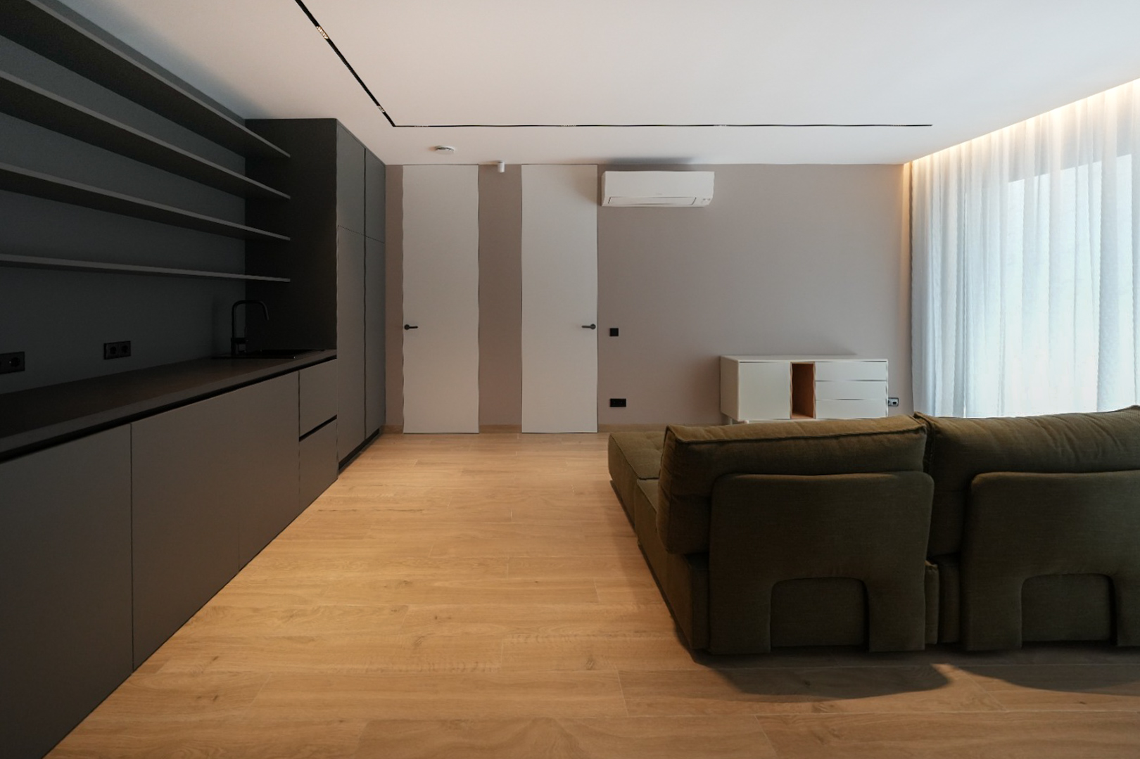 Espacio de vida moderno con cocina integrada en gris oscuro, suelo de madera clara y sofá modular verde. Puertas enrasadas y luz natural. Espacio de vida moderno con cocina integrada en gris oscuro, suelo de madera clara y sofá modular verde. Puertas enrasadas y luz natural.
