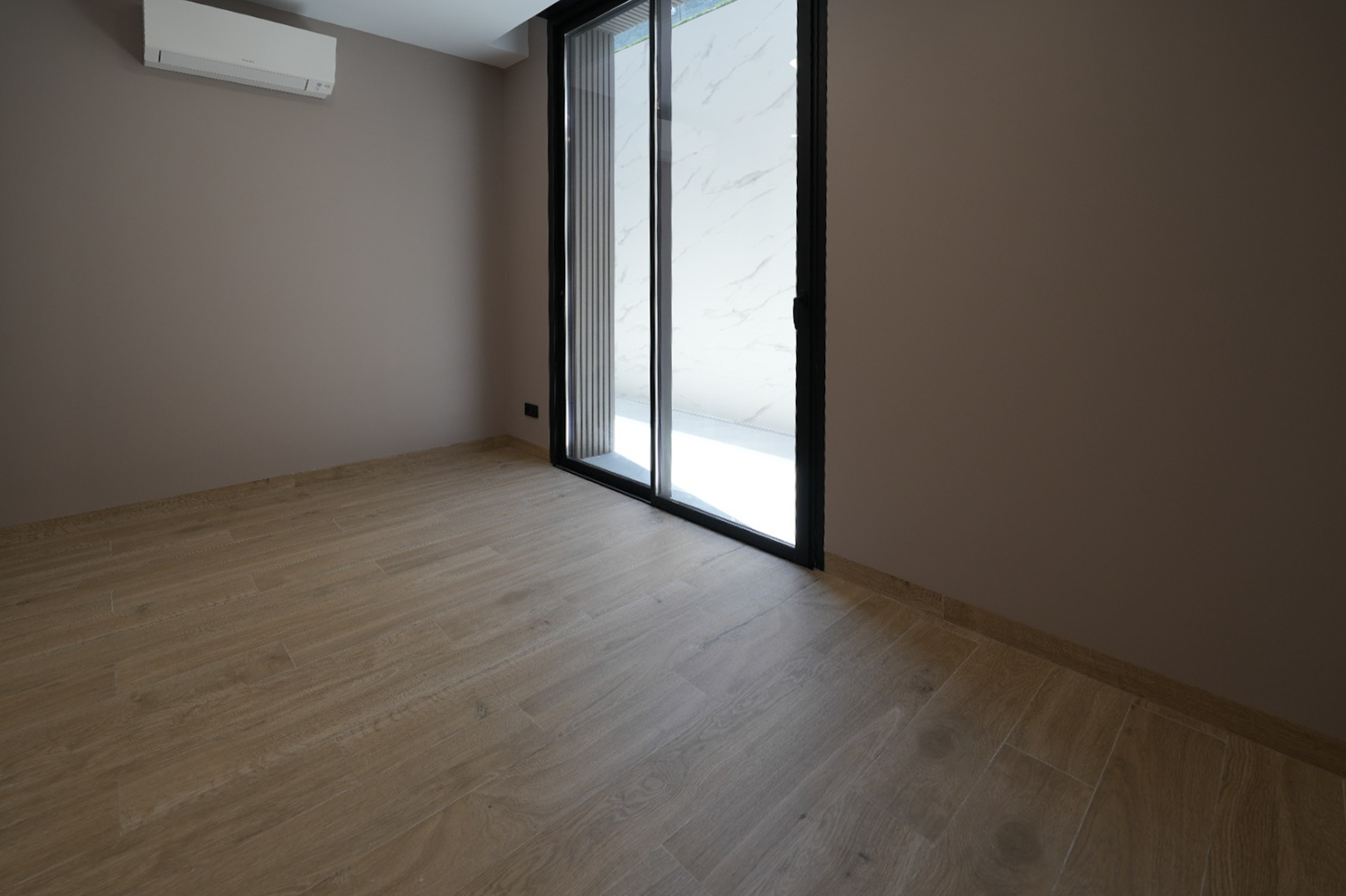 Habitación diáfana con suelo de gres porcelánico imitación madera, paredes en tono topo y puerta corredera de cristal con marco negro. Incluye unidad de aire acondicionado. Habitación diáfana con suelo de gres porcelánico imitación madera, paredes en tono topo y puerta corredera de cristal con marco negro. Incluye unidad de aire acondicionado.