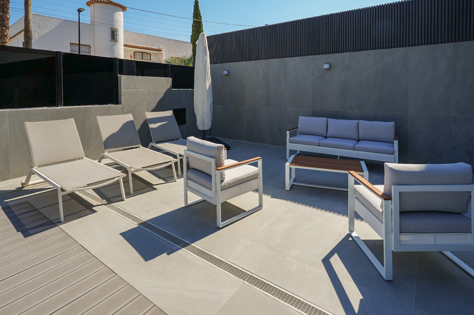 Terraza exterior con mobiliario de diseño en tonos neutros, combinando gres porcelánico y tarima de composite. Incluye tumbonas y zona de estar con sofá y sillones. Terraza exterior con mobiliario de diseño en tonos neutros, combinando gres porcelánico y tarima de composite. Incluye tumbonas y zona de estar con sofá y sillones.