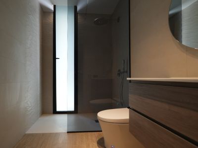 Baño moderno con mueble de madera, espejo redondo y ducha a ras de suelo. Destacan azulejos texturizados y una ventana esmerilada.