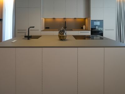 Cocina de diseño con isla central, fregadero integrado, placa de inducción y mobiliario en tonos neutros.