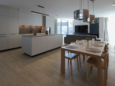 Cocina de diseño minimalista con isla central y grifería negra, abierta a un elegante comedor de madera con seis sillas y lámparas colgantes modernas.