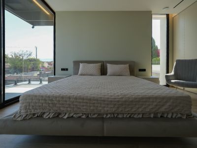 Dormitorio principal con cama flotante, cabecero tapizado, grandes ventanales con vistas al mar y sillón. Mesitas de noche integradas.