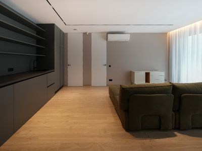 Espacio de vida moderno con cocina integrada en gris oscuro, suelo de madera clara y sofá modular verde. Puertas enrasadas y luz natural.