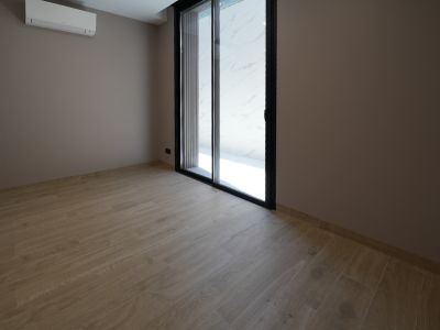 Habitación diáfana con suelo de gres porcelánico imitación madera, paredes en tono topo y puerta corredera de cristal con marco negro. Incluye unidad de aire acondicionado.