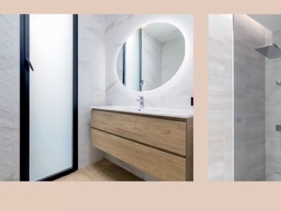 Moderno baño con lavabo flotante de madera, espejo ovalado iluminado y ducha de lluvia. Paredes de mármol y azulejos texturizados.